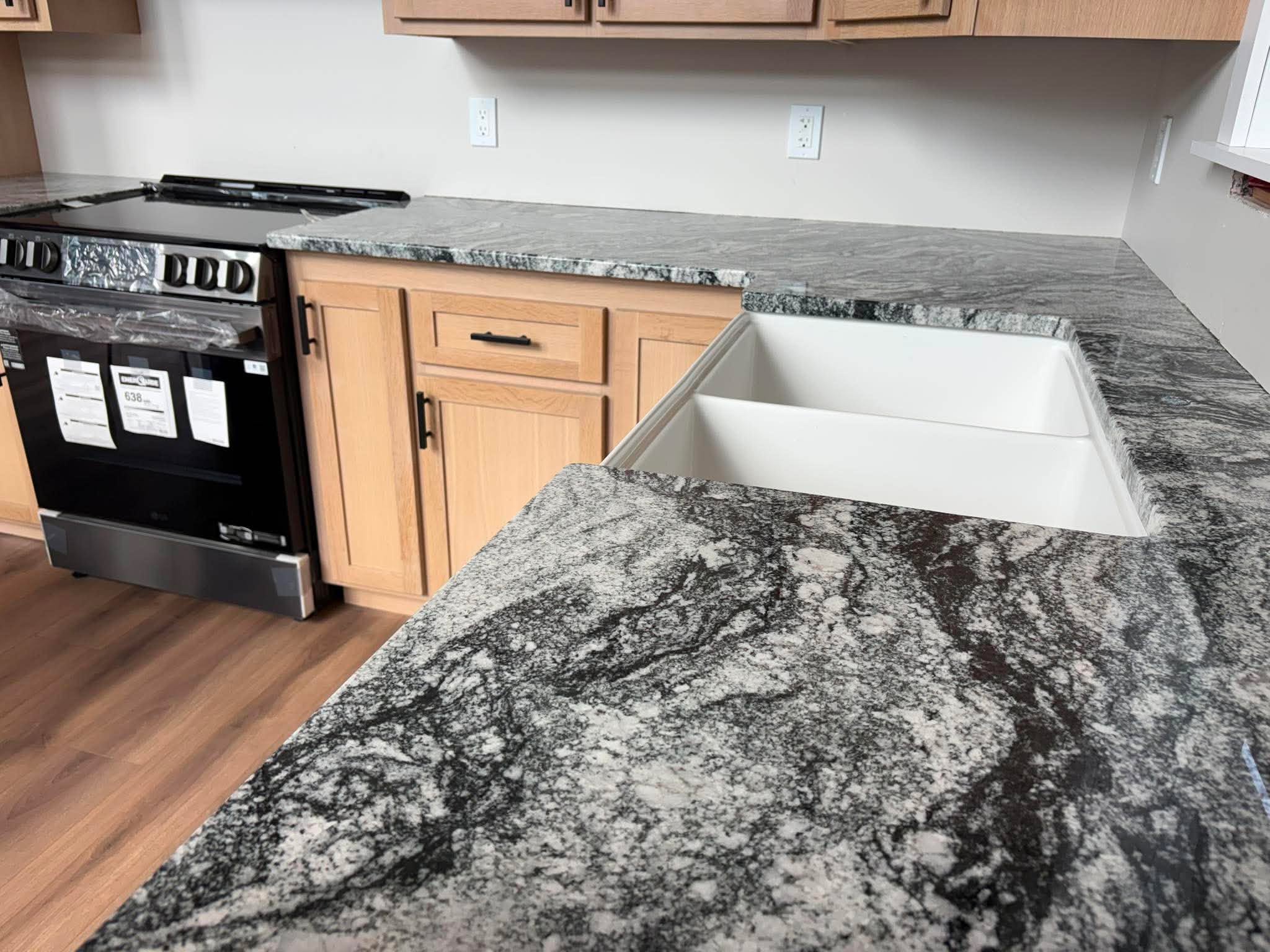 Dark granite countertop surface seen from behind showing dramatic swirling veining, range and farmhouse sink.