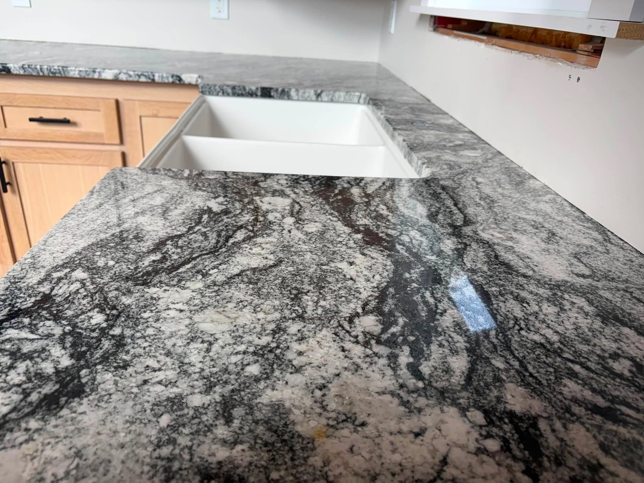 Close-up of dramatic black, grey and white swirling granite countertop surface beside farmhouse sink.