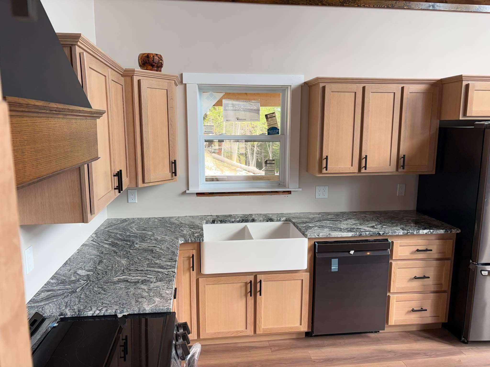Completed kitchen — dark swirling granite countertops across the full L-shaped run, oak cabinetry with matte-black hardware, white farmhouse sink and black range hood.