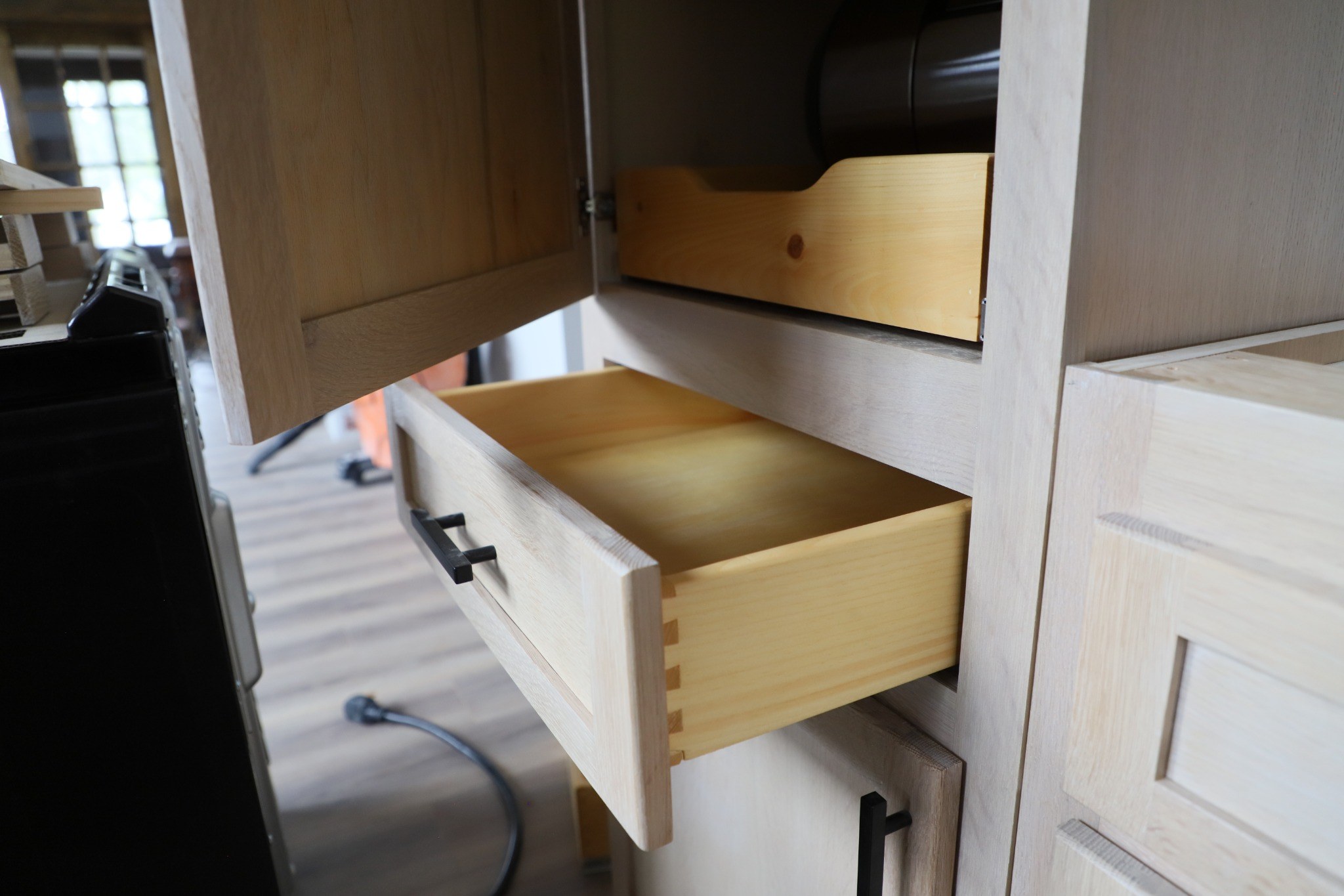 Open solid-wood drawer with visible dovetail joinery inside a natural wood cabinet.