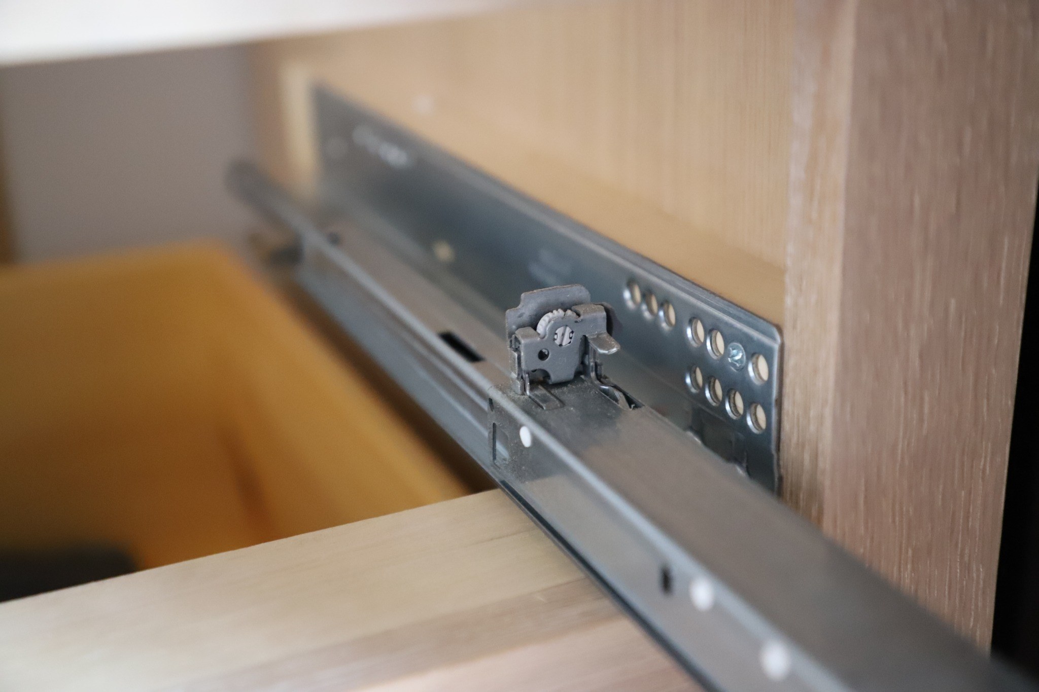 Close view of the metal drawer-slide hardware inside a natural wood cabinet.