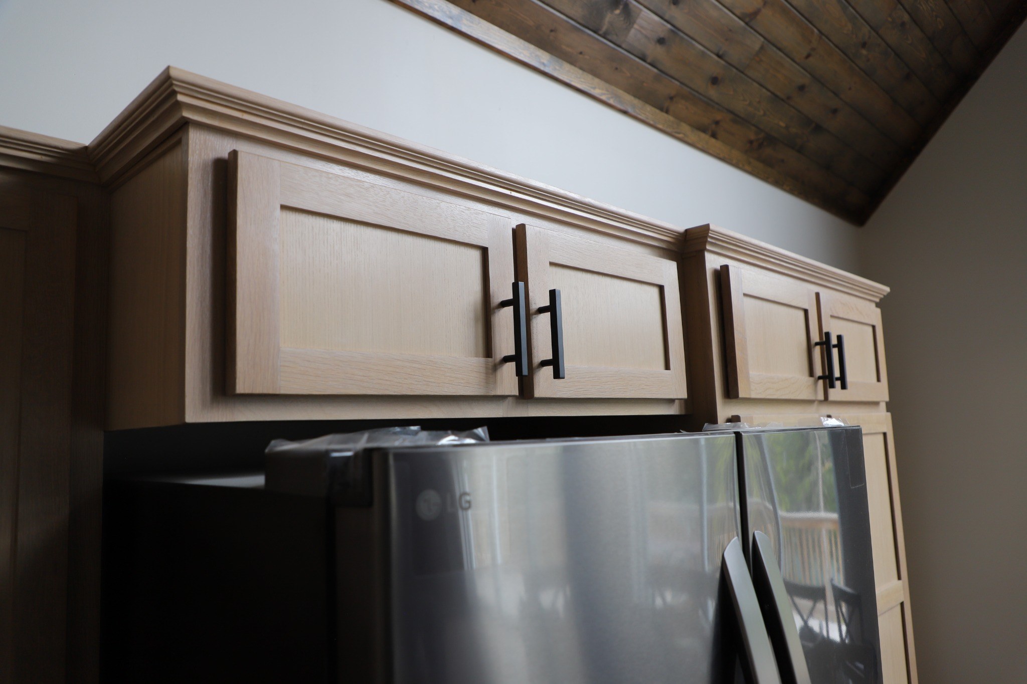 Natural wood upper cabinets with black pulls installed above a refrigerator opening.
