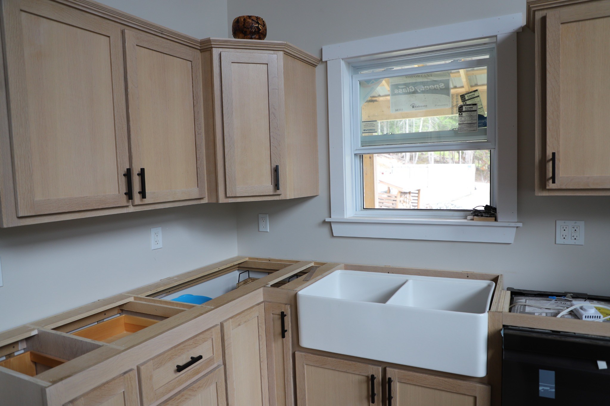 Natural wood kitchen cabinetry — upper and lower cabinet runs with matte-black hardware installed before countertop templating.
