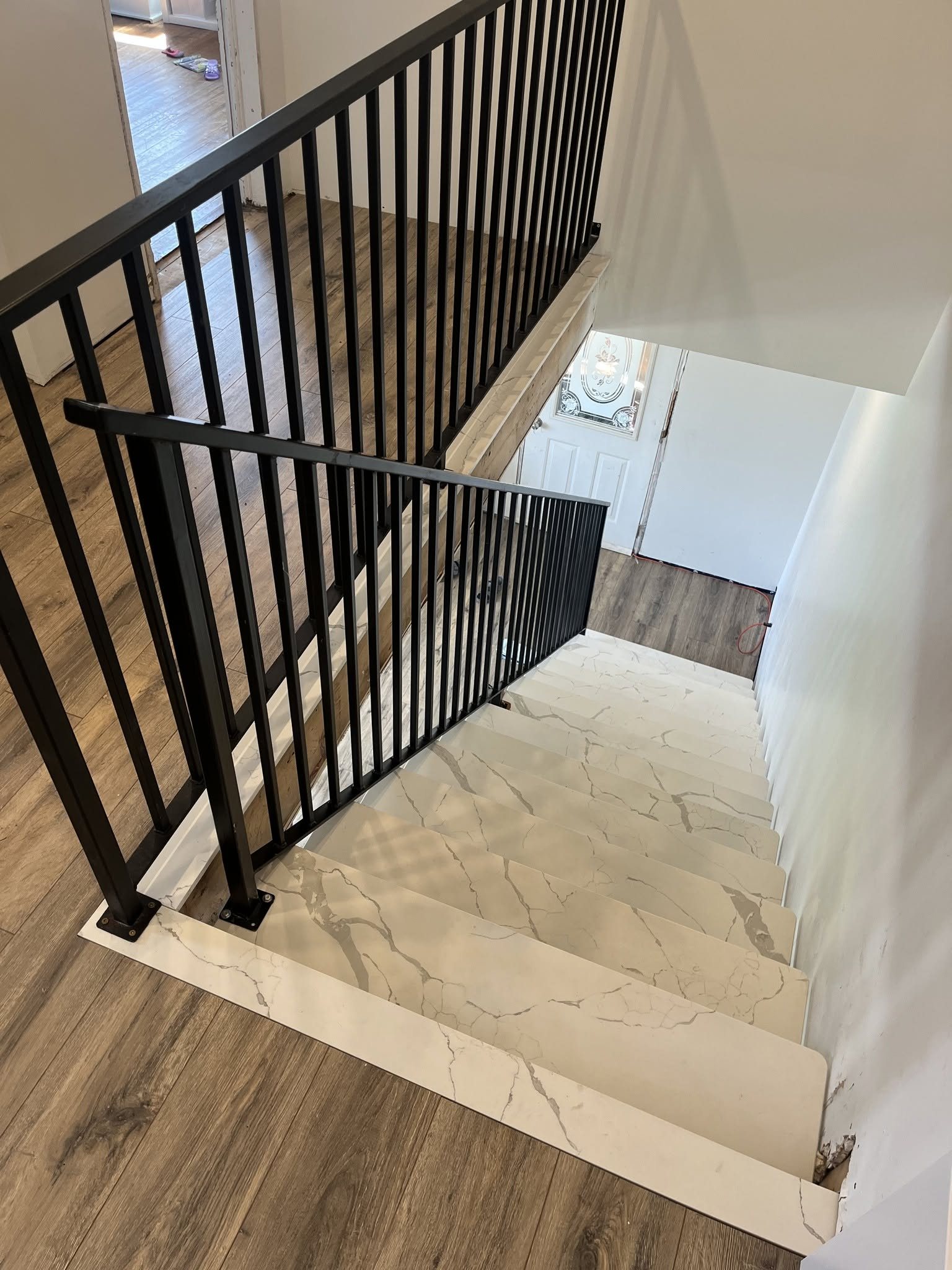 Residential staircase finished with light stone treads and black metal railings.