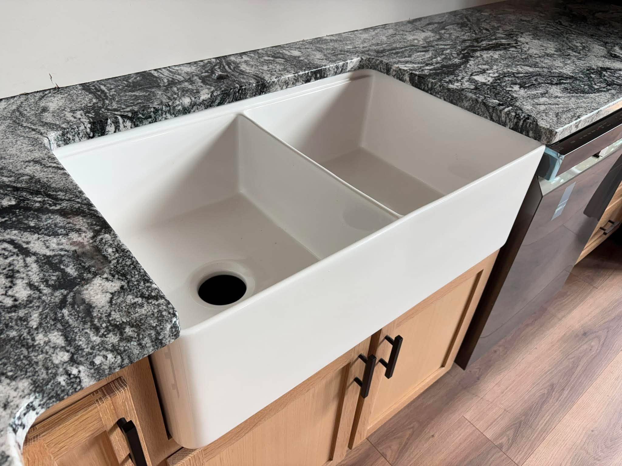 Farmhouse sink set into a dark granite countertop, fabricated and installed by Oak Bay Rock & Tile.