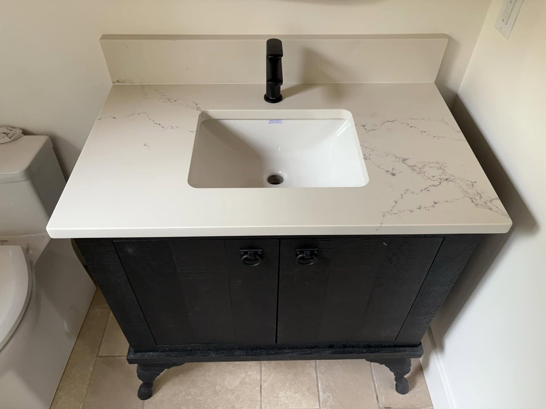 Compact bathroom vanity with white quartz surface and dark antique cabinet, finished by Oak Bay Rock & Tile.