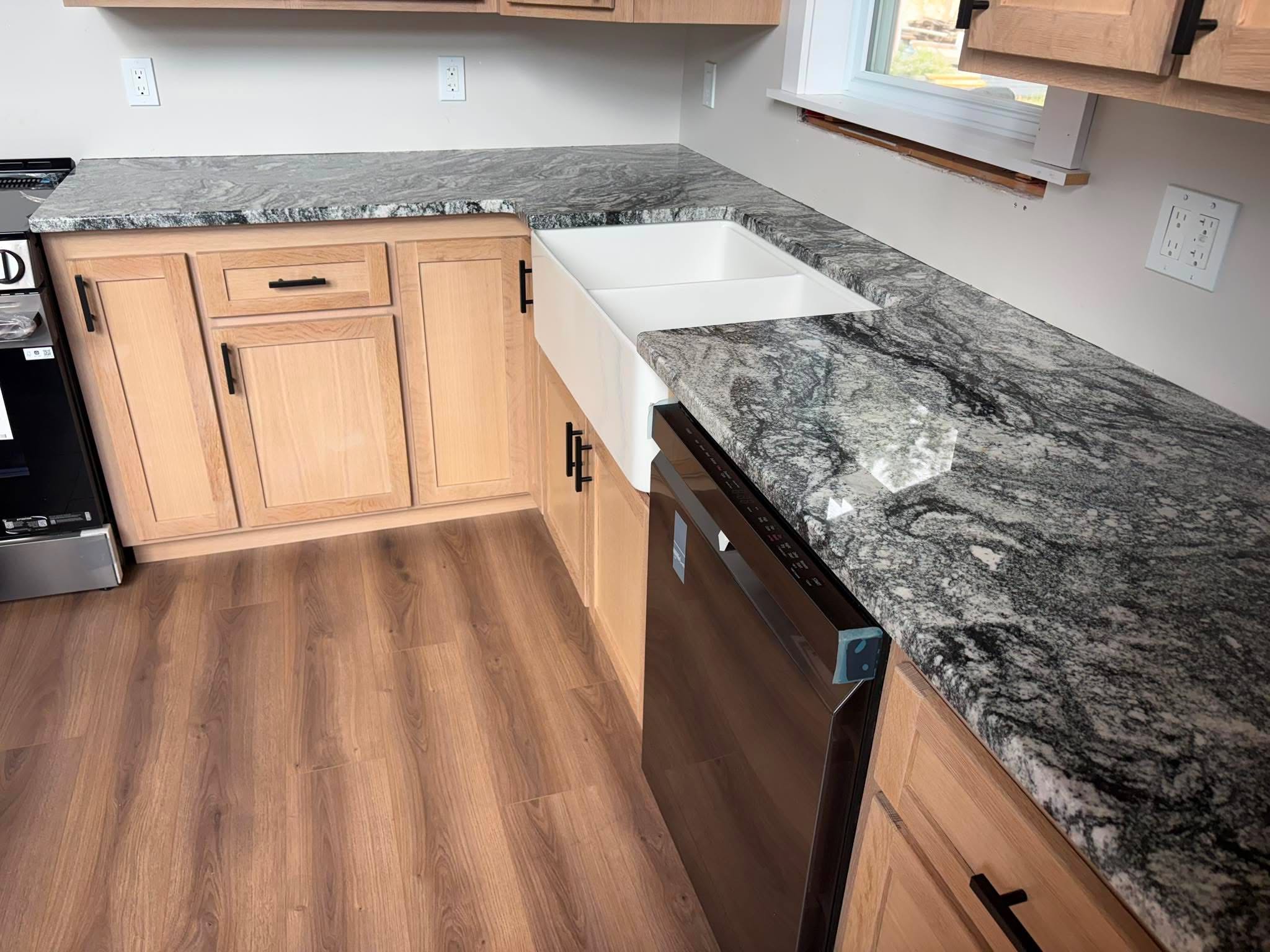 Patterned granite countertop run with white farmhouse sink set into a natural wood kitchen — view from the side during installation.